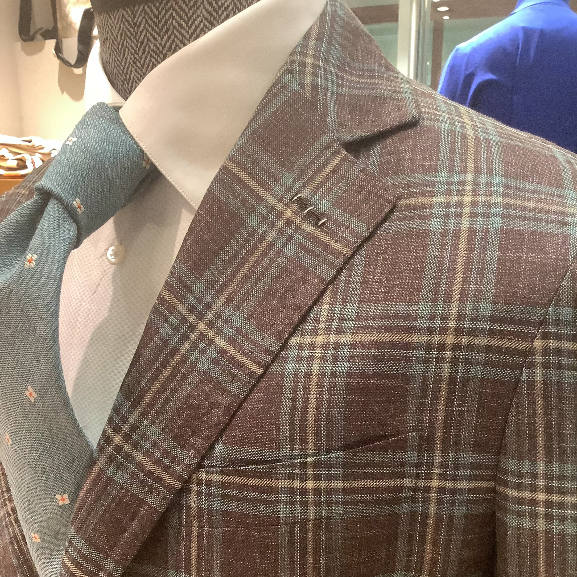A tailored jacket with a notch lapel, featuring a brown and blue plaid pattern, displayed on a mannequin.